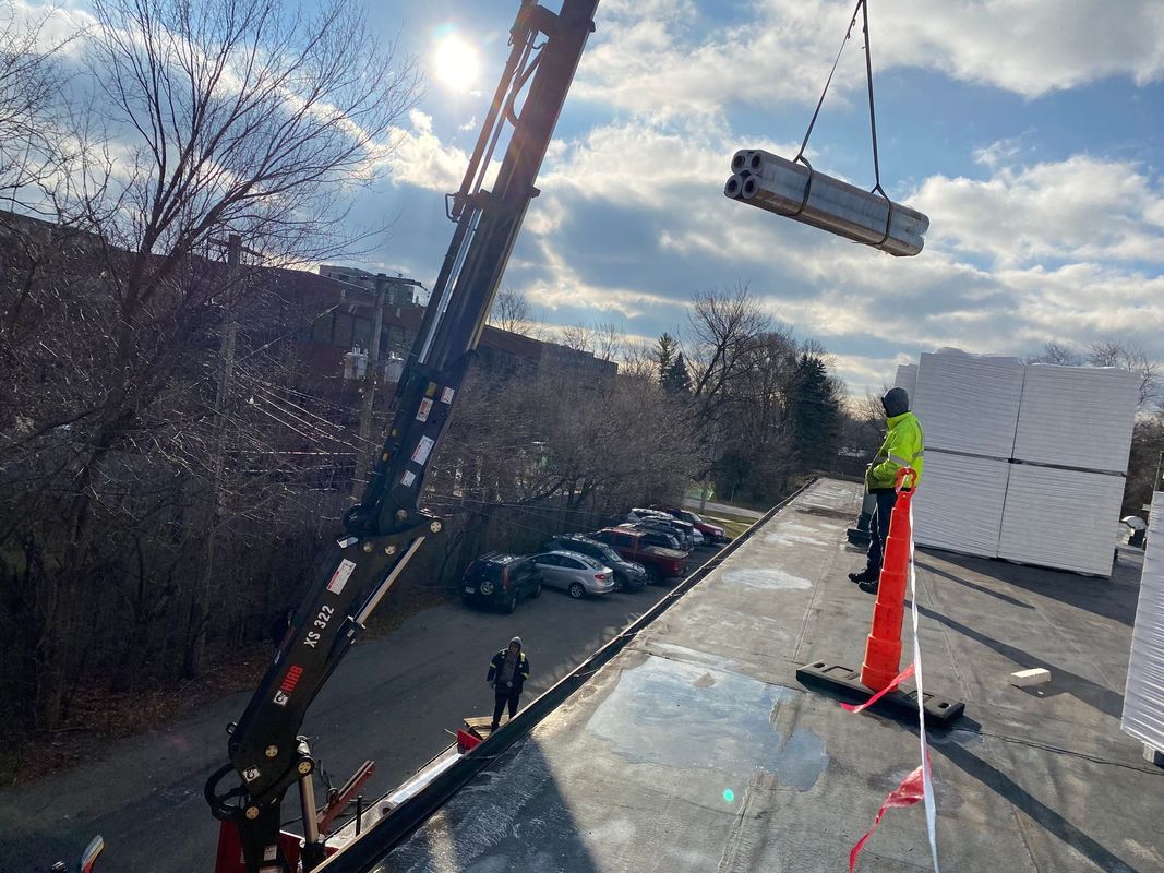 Crane lifting equipment to rooftop where workers install it. Blue sky.