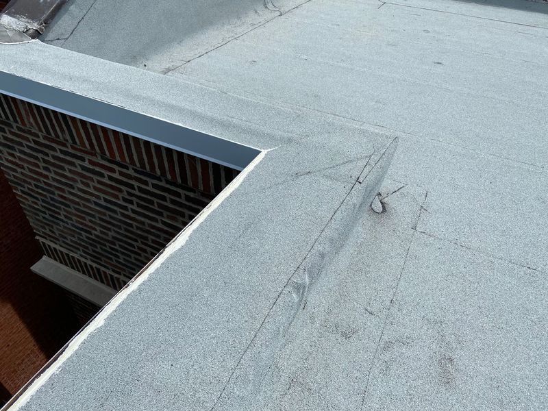 Flat roof corner with metal flashing and brick wall.