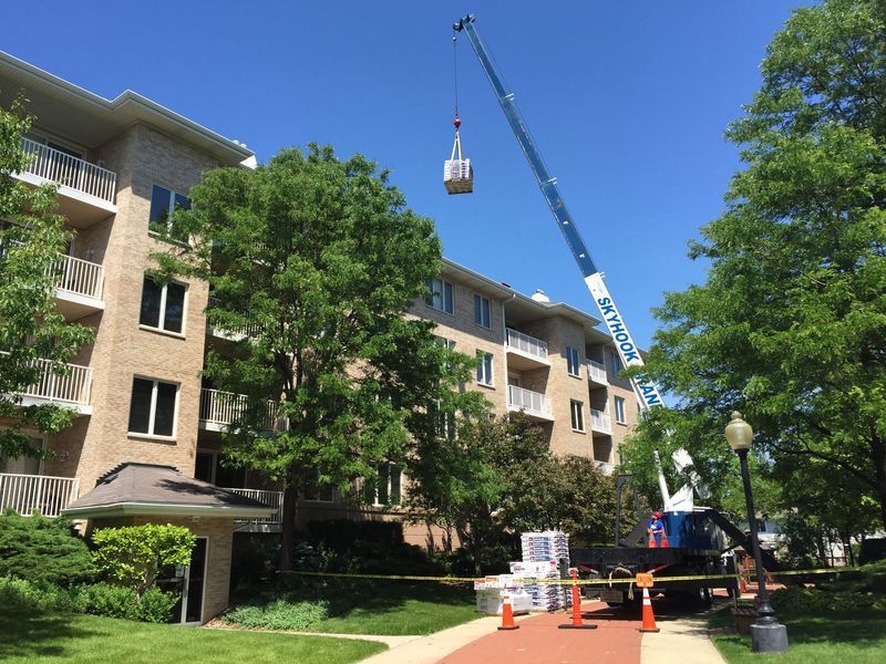 Crane lifting equipment onto a multi-story building on a sunny day.