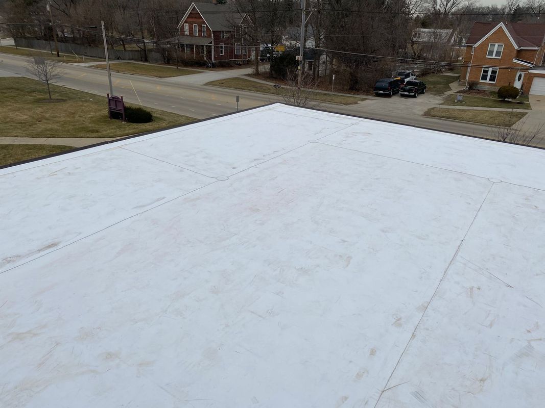 White flat roof with visible seams, buildings and street in background.