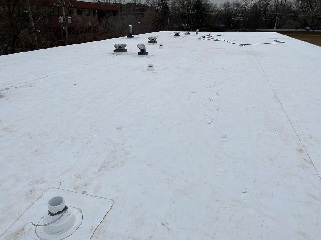 White, flat commercial roof with various vents and protrusions. Gray sky in the background.