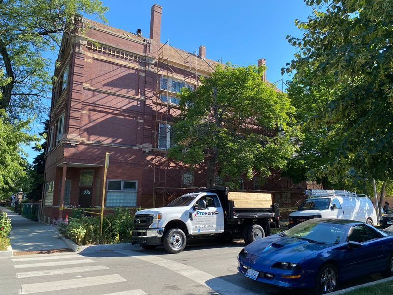 Building with scaffolding, a truck, and a parked blue car on a street corner.