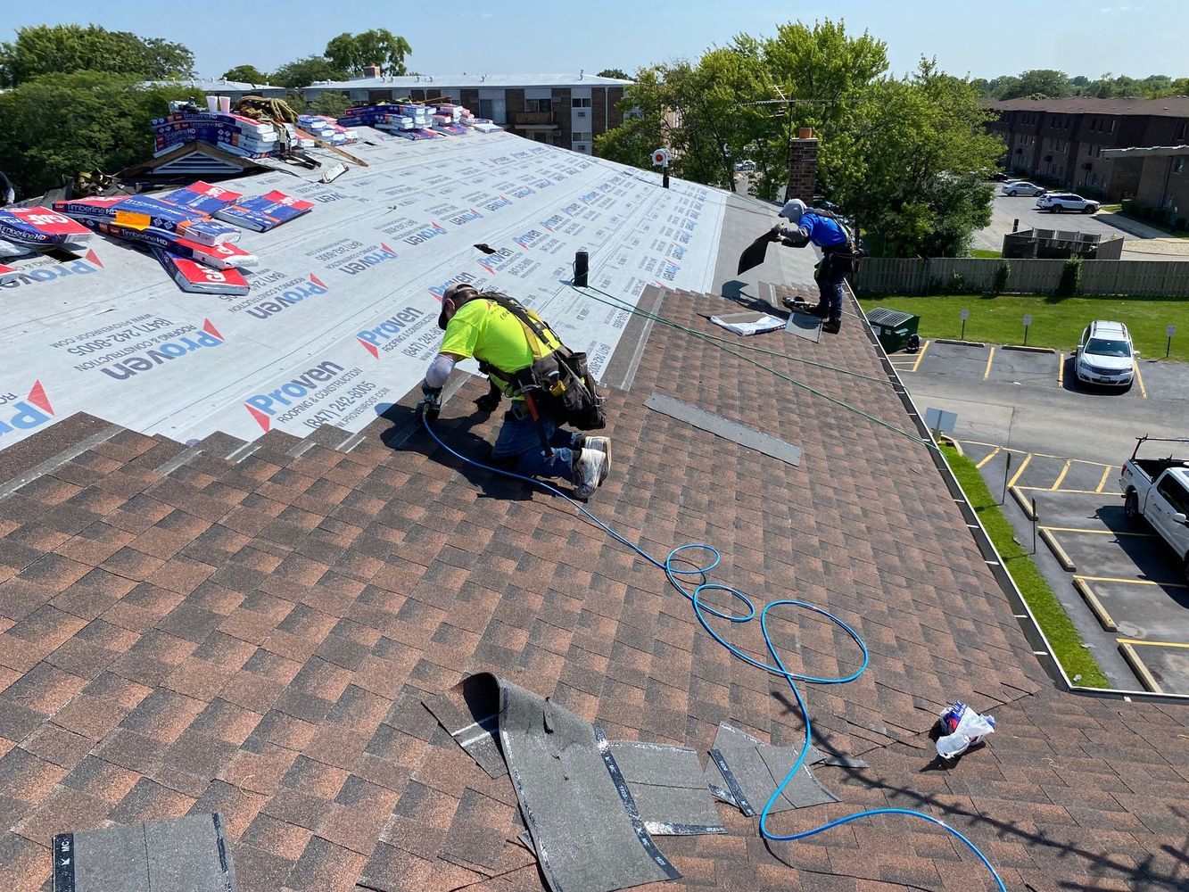 Roofers installing shingles on a residential building on a sunny day.