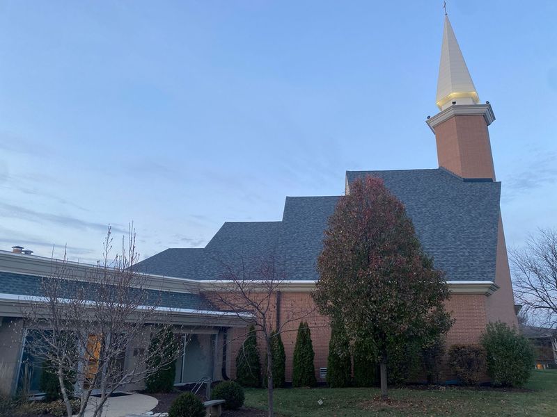 A peach-colored church with a steeple, set against a blue sky, some trees in front.