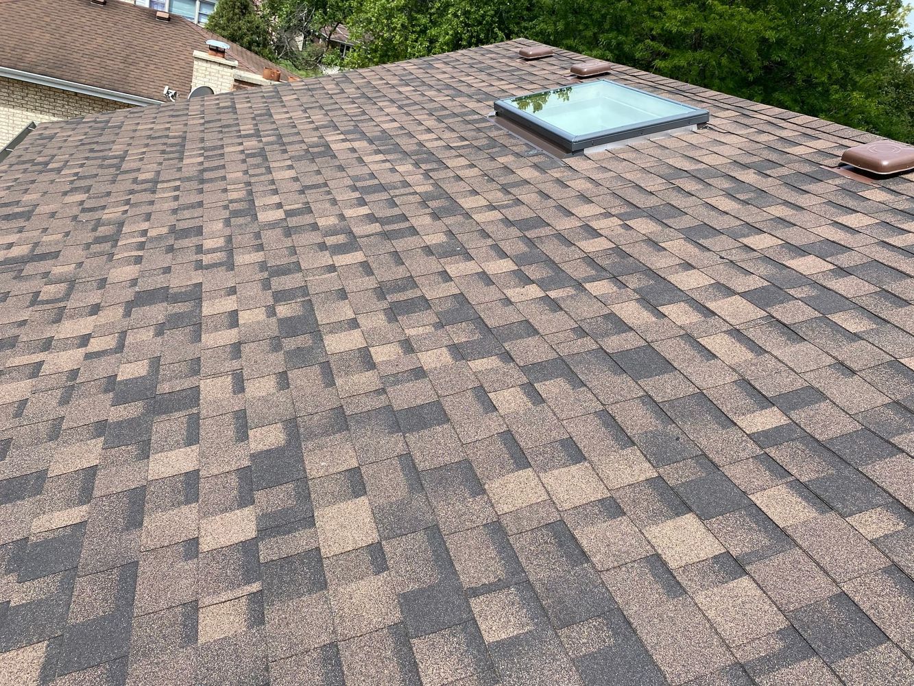 Brown and black asphalt shingle roof with a rectangular skylight.
