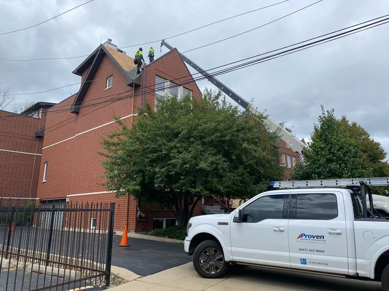 Workers on a church roof with a crane; a white truck is parked nearby.