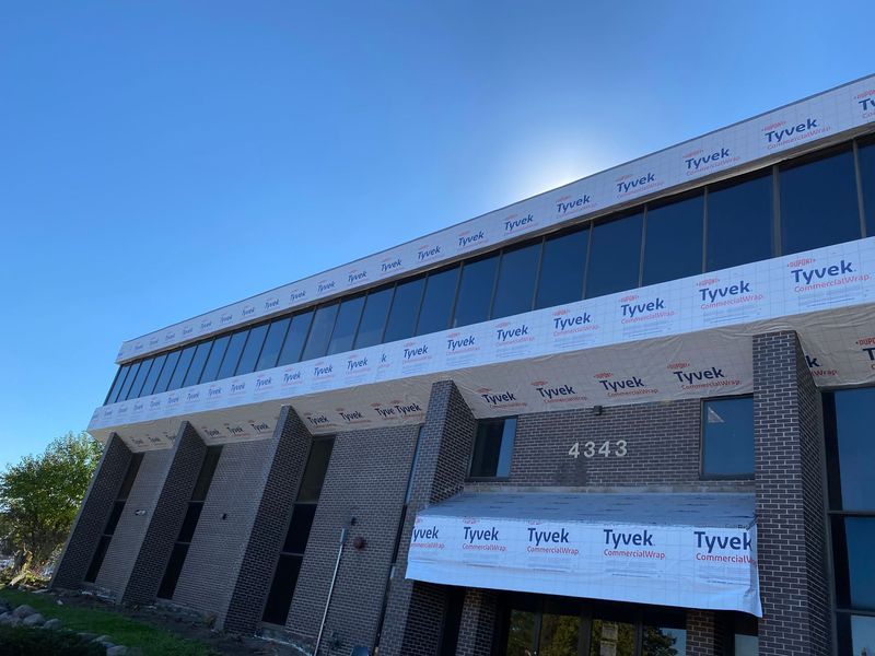 A two-story brick building under construction with many large windows, bright sky. 