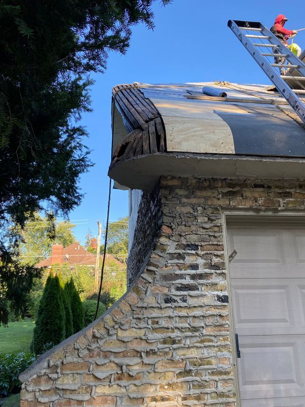 Roof under construction with person on ladder, building with brick facade.