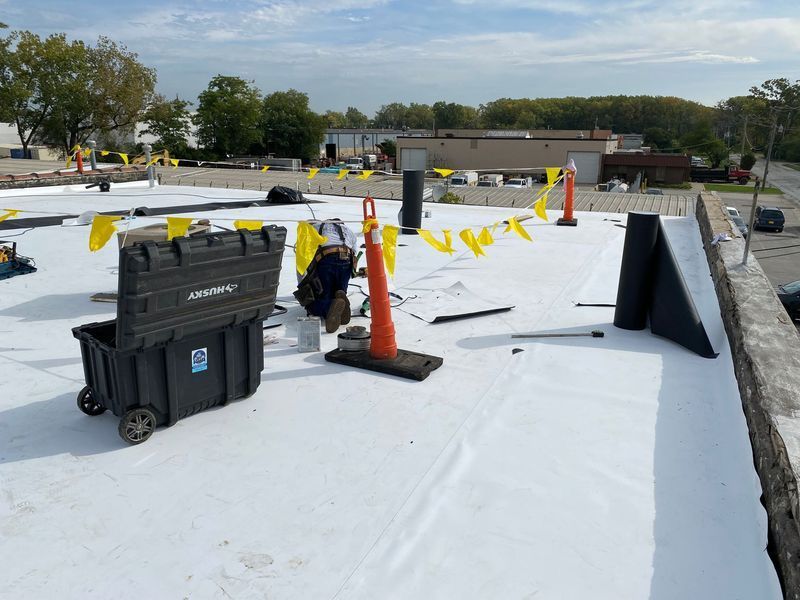 Roofing construction scene: White flat roof with tools, safety cones, and caution flags.