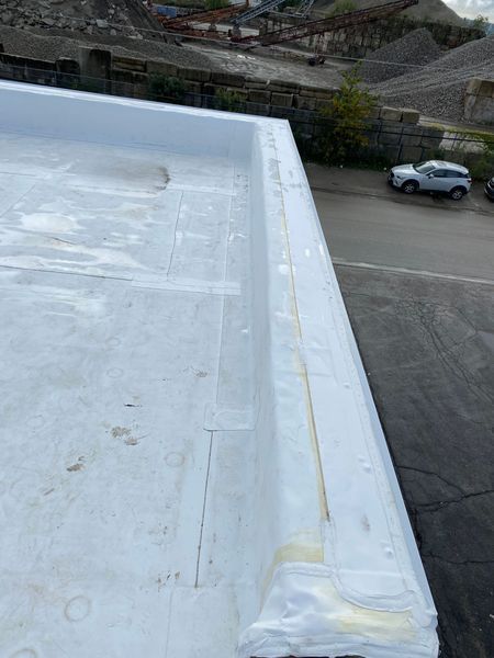 White rooftop with raised edge, next to a road, and parked vehicle. Industrial setting in background.