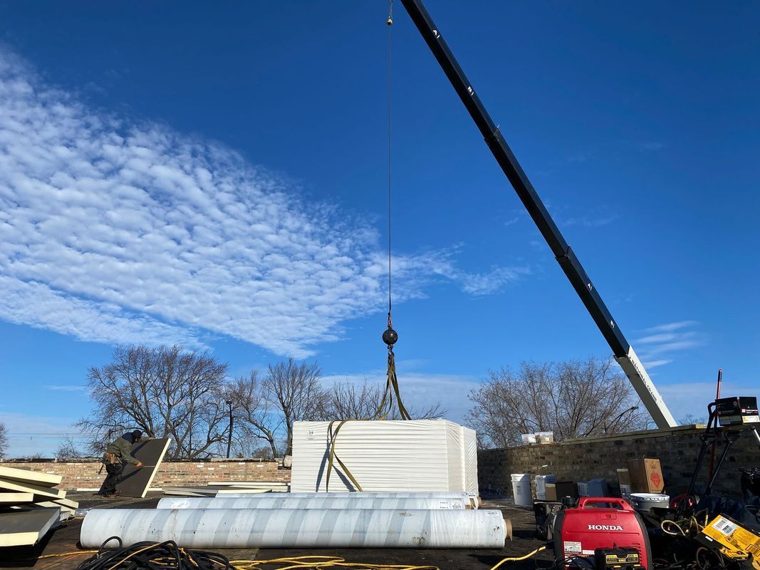 Crane lifting a stack of white building materials against a blue sky with wispy clouds.