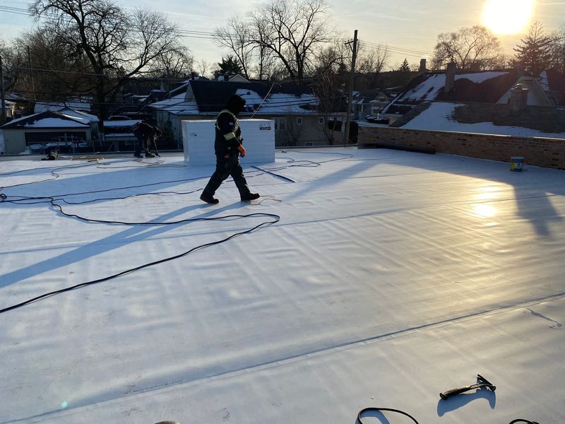 Person walking on a flat, white roof during construction. The sun is shining.