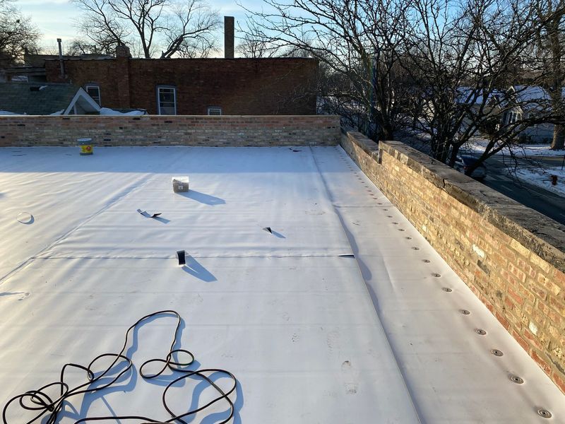 Flat white roof with a brick wall, tools scattered, and buildings in the background.