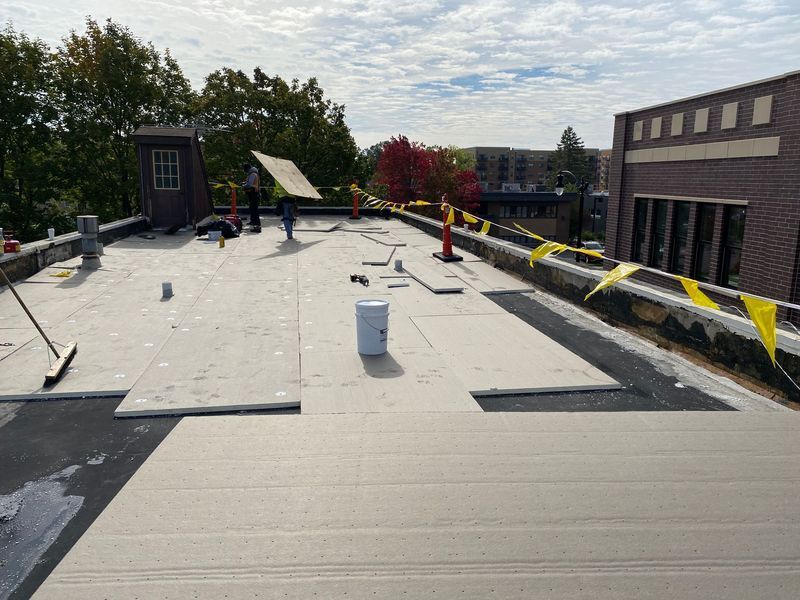 Roofing crew on a flat roof, installing new material under a cloudy sky.