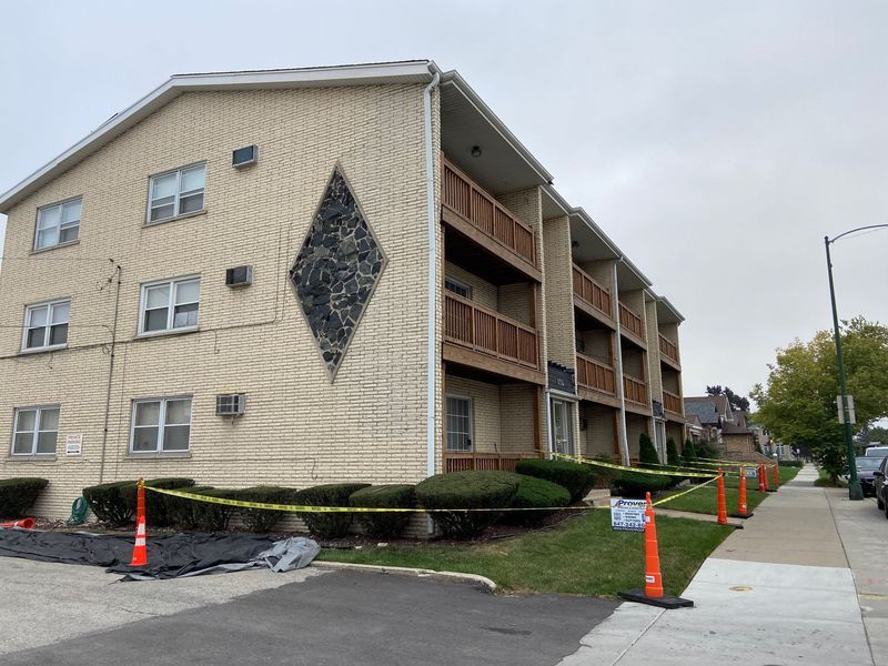 Apartment building with diamond-shaped design on the brick facade. Caution tape lines the sidewalk. Overcast day.