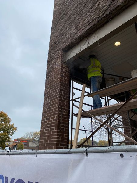 Construction worker on scaffolding, repairing brick building exterior. Worker wears a high-visibility vest.