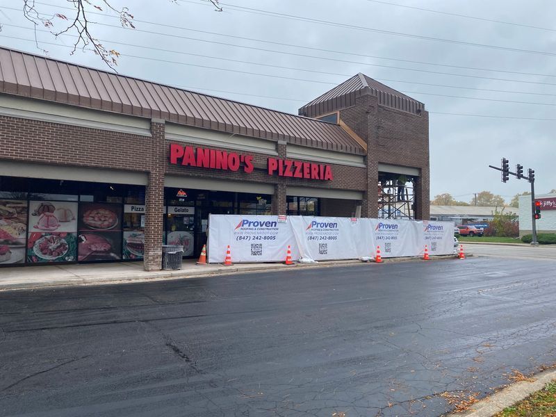 Panino's Pizzeria building with temporary construction barriers. Red signage, brick exterior, overcast day.