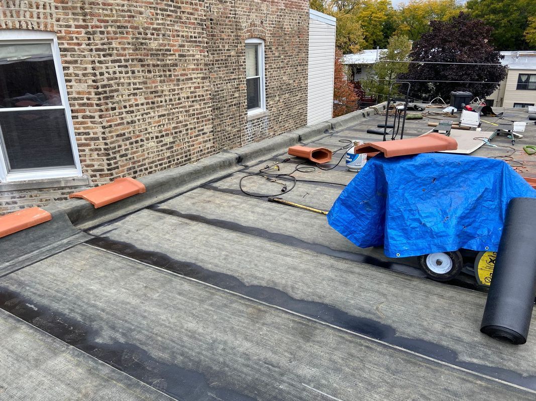 Flat roof with brick building, tools, and a blue tarp.