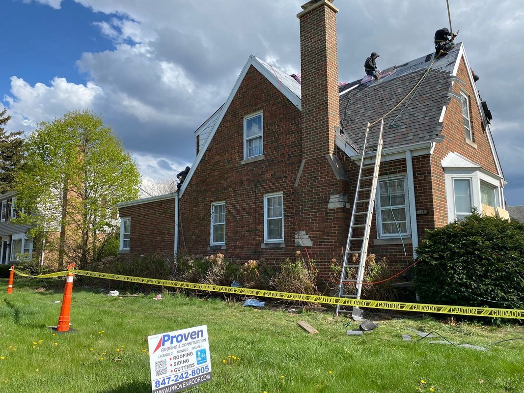Brick house with roof repair in progress; workers on roof, ladder against the side.
