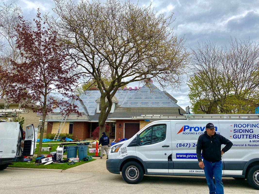 A roofing company's van parked in front of a house, workers on site, partially completed roof.
