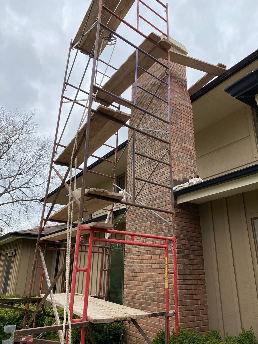 Scaffolding next to a tall brick chimney on a house, under a cloudy sky.