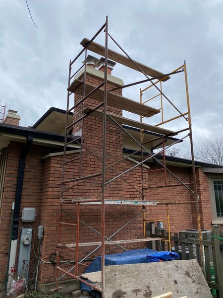 Scaffolding next to a brick chimney, likely for repair work. Overcast sky.