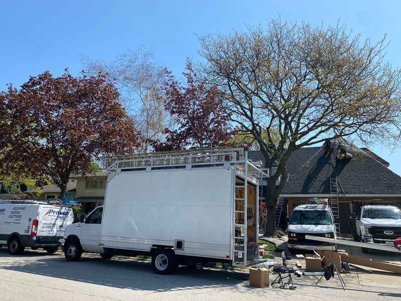 Truck with canvas sides parked by house; workers on roof.