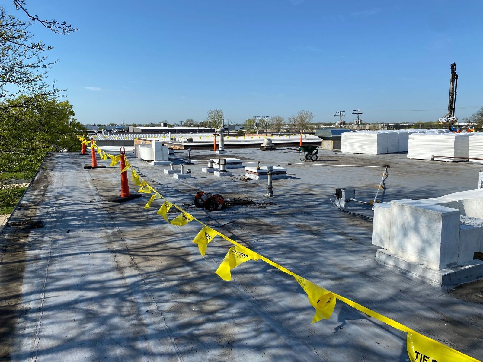 Rooftop with construction materials and yellow caution tape on a sunny day.