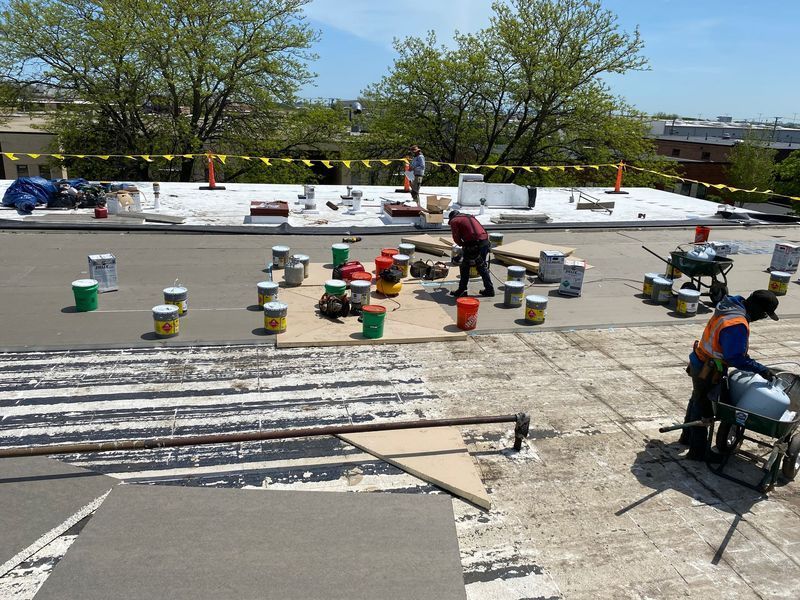 Roofing crew working on a flat roof under a blue sky, surrounded by tools and materials.