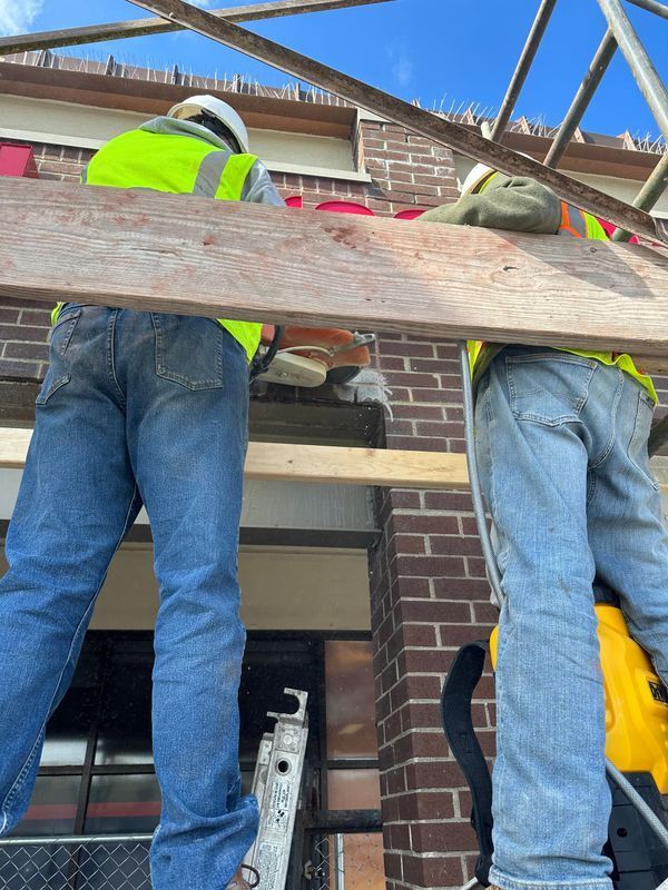 Construction workers using power tools on brick building, under clear blue sky.