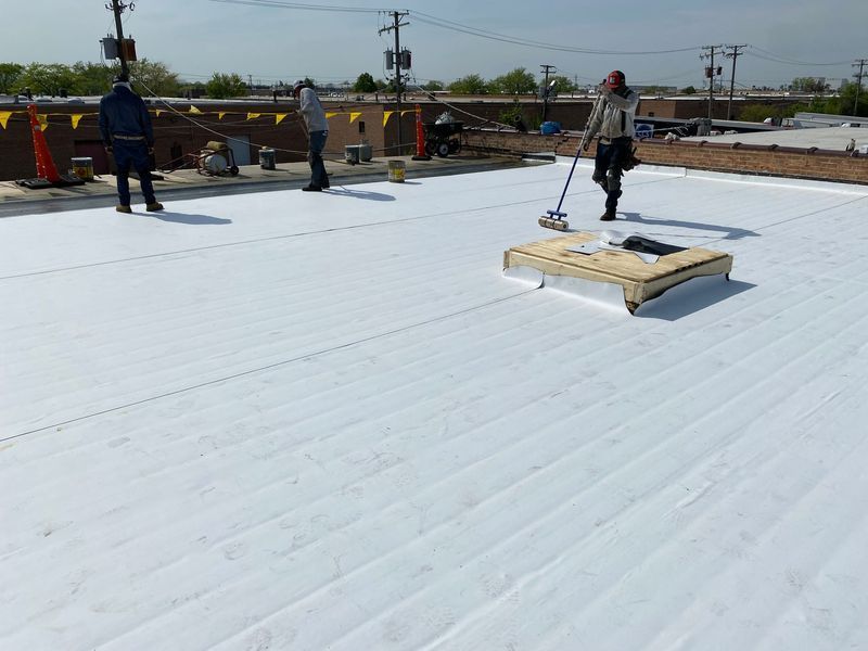 Workers installing white roofing material on a flat roof on a sunny day.