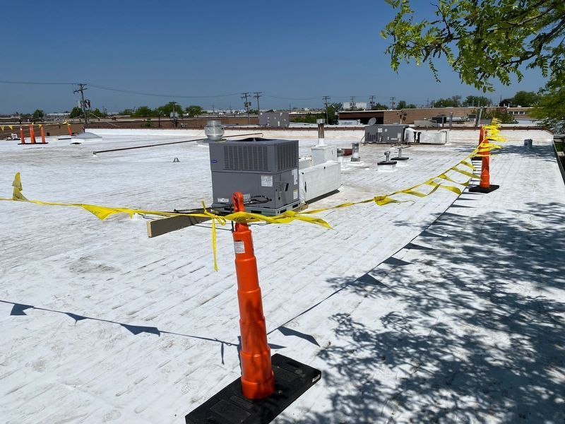 White roof with HVAC units; yellow caution tape strung between orange pylons.