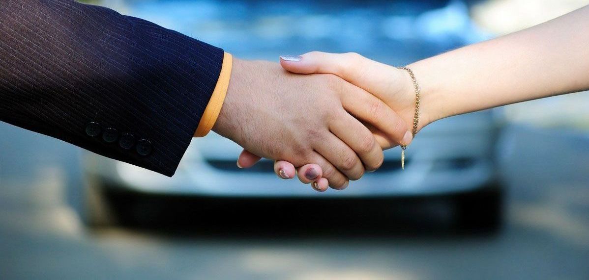 A man and a woman are shaking hands in front of a car.