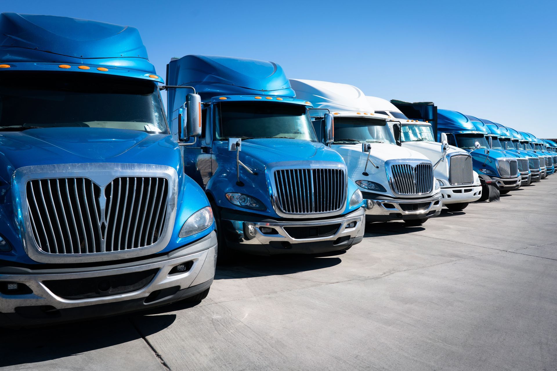 A row of blue semi trucks are parked in a parking lot.