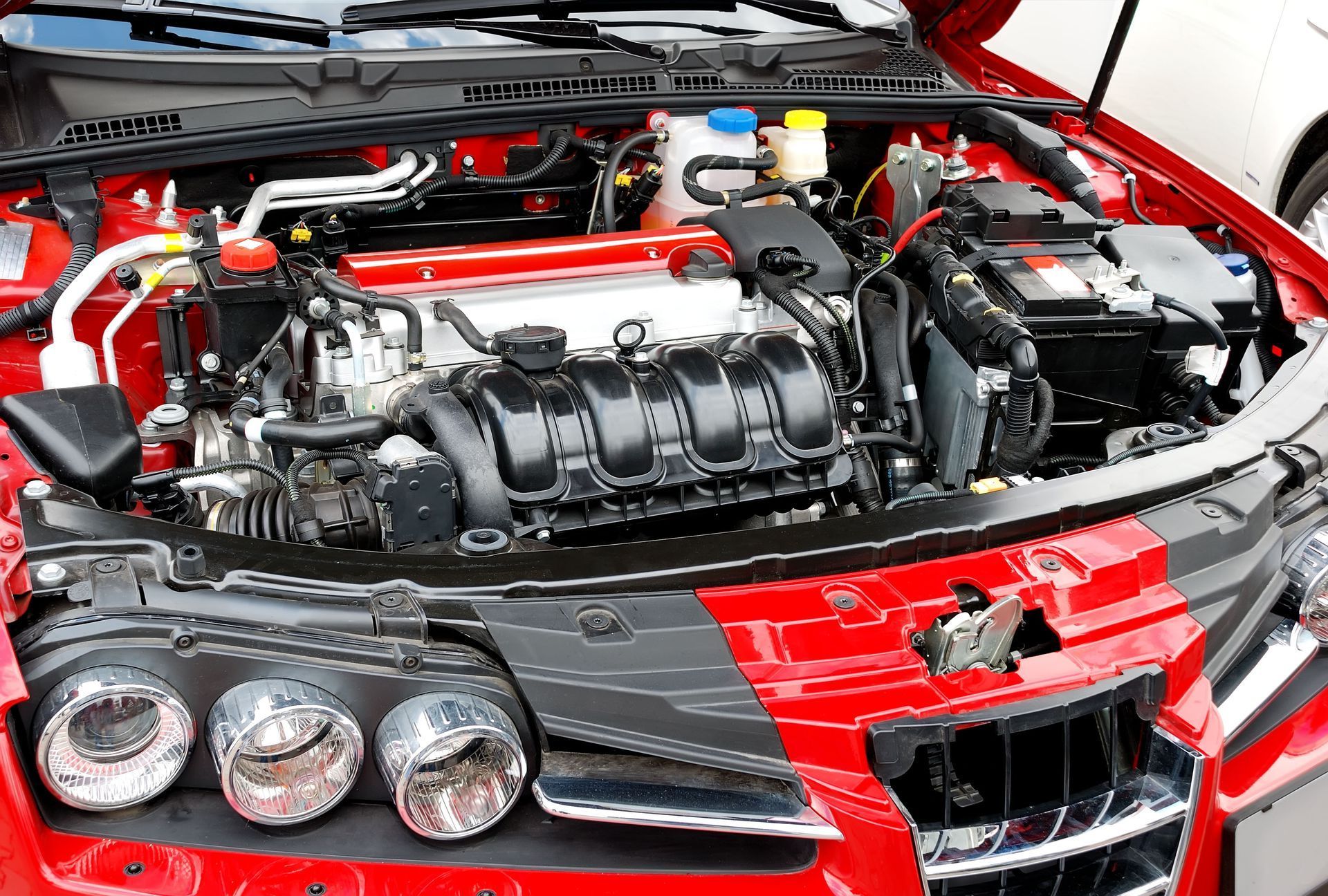 The engine of a red car is visible under the hood.