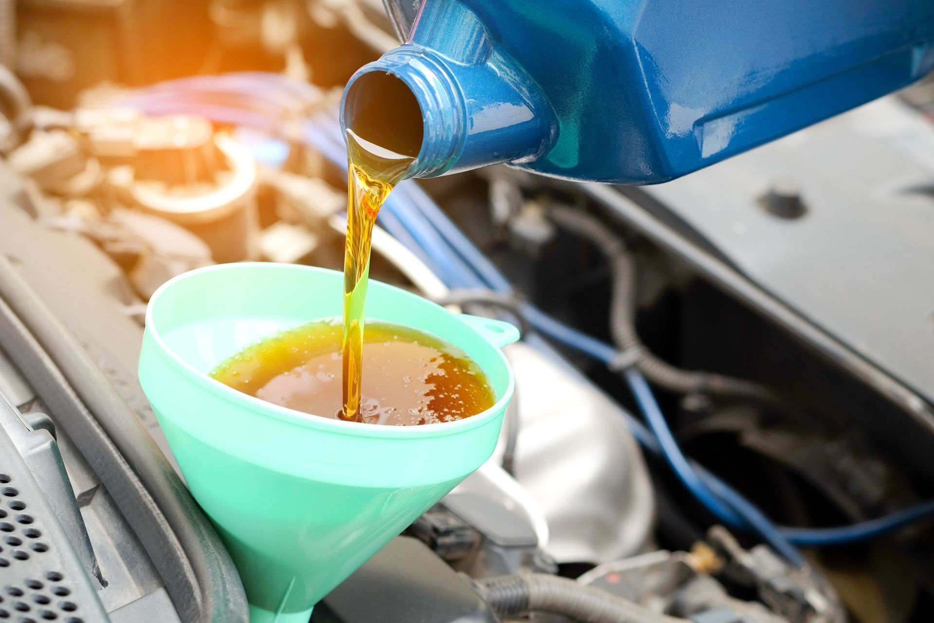 A person is pouring oil into a funnel from a bottle.
