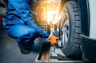Mechanic in blue jumpsuit, orange gloves, inspecting car tire in a garage, using alignment equipment