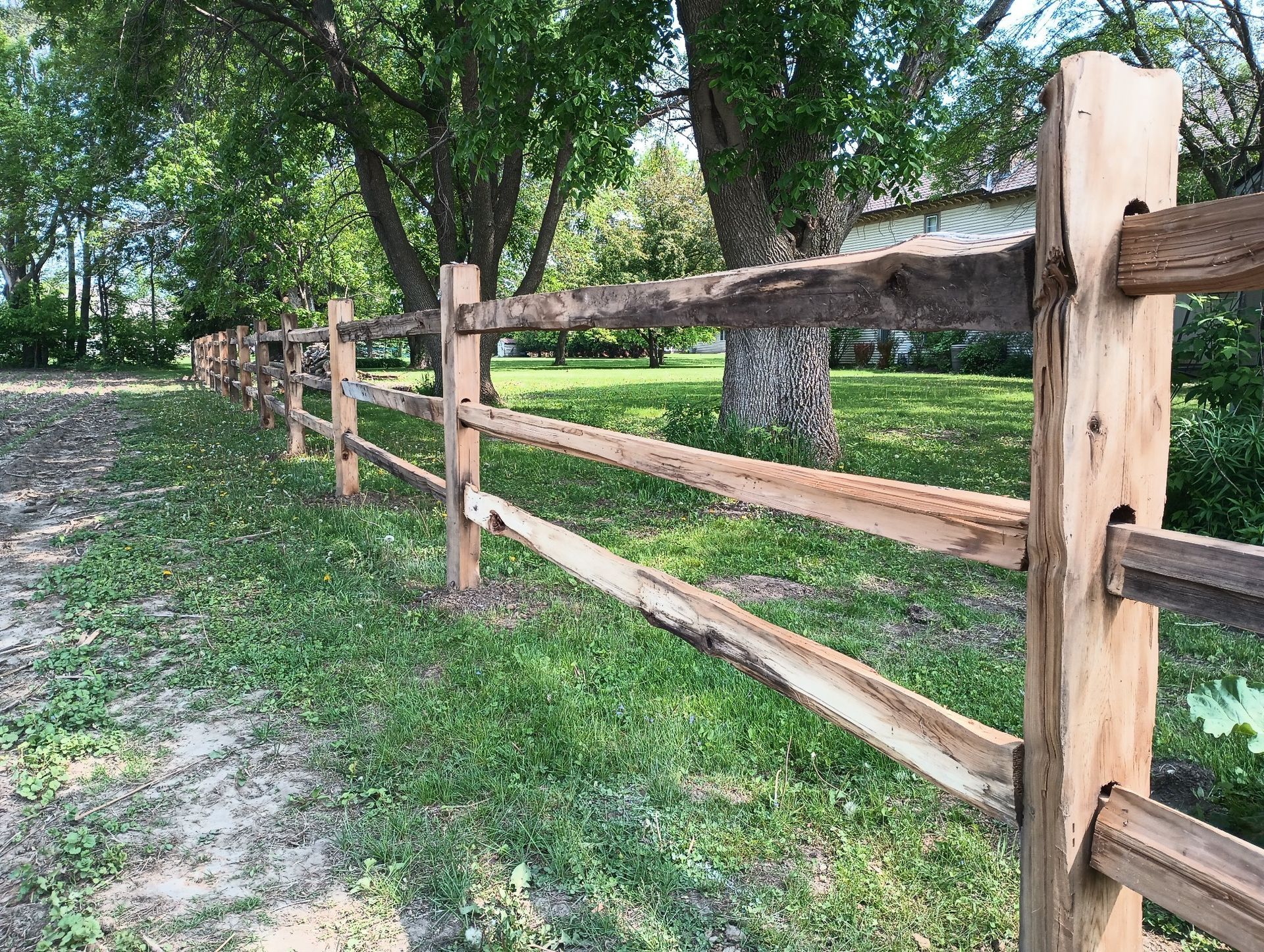 A wooden fence surrounds a grassy field next to a dirt road.