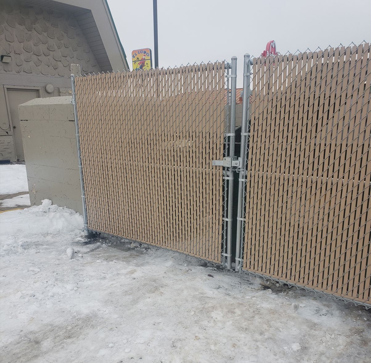 A chain link fence is surrounded by snow and a building