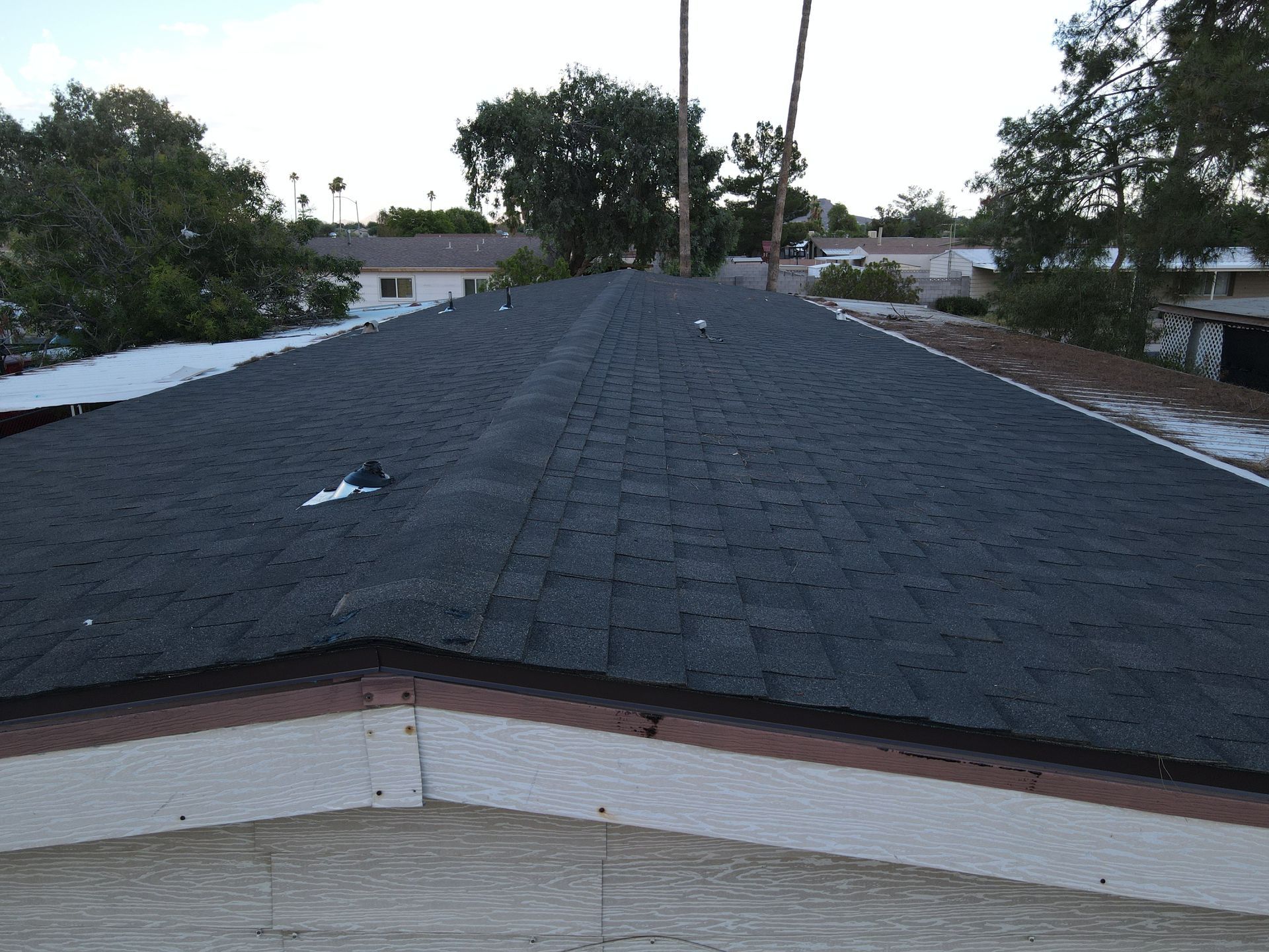 A black roof with a white trim and trees in the background.
