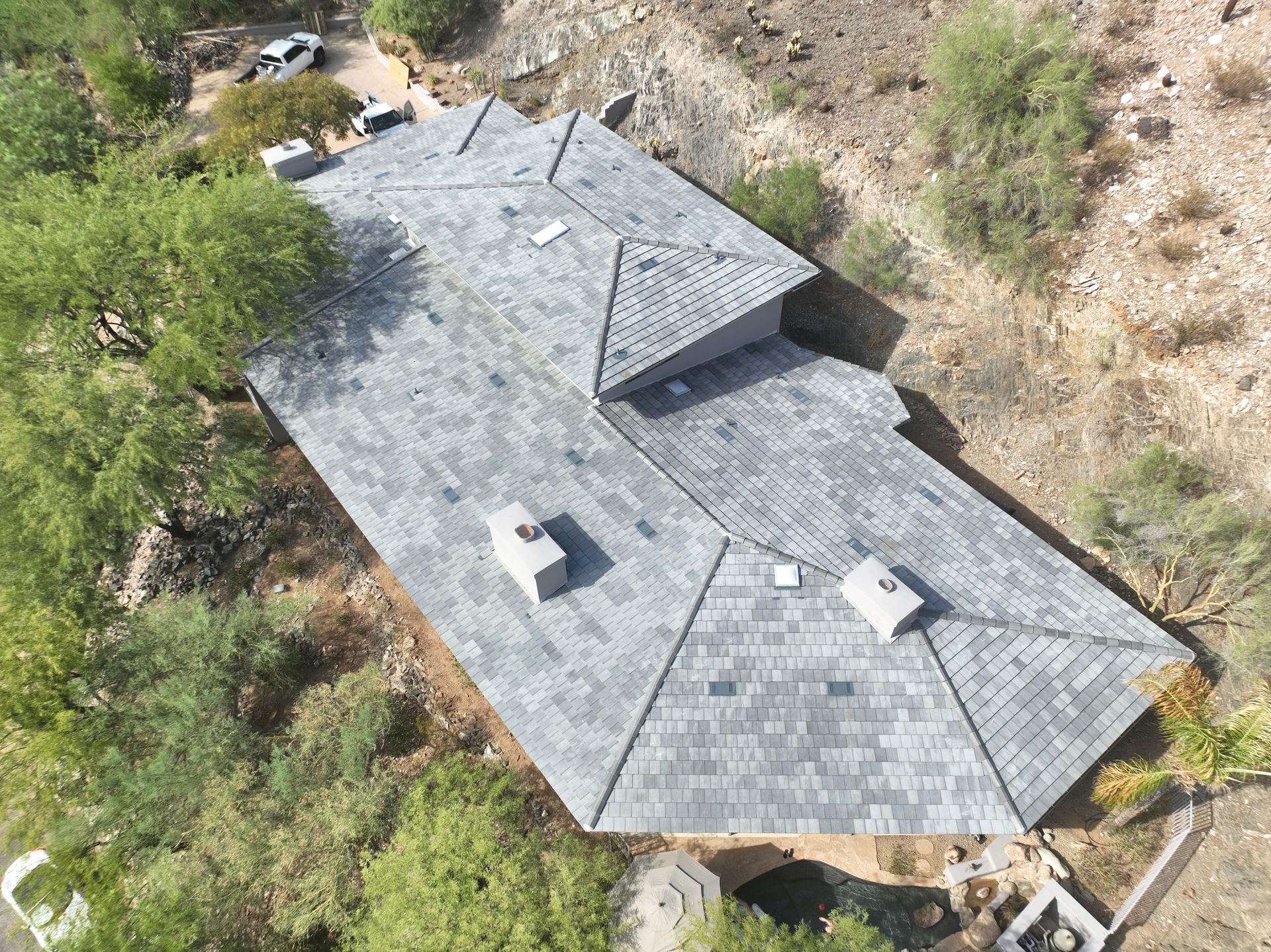 An aerial view of a house with a roof that is surrounded by trees.