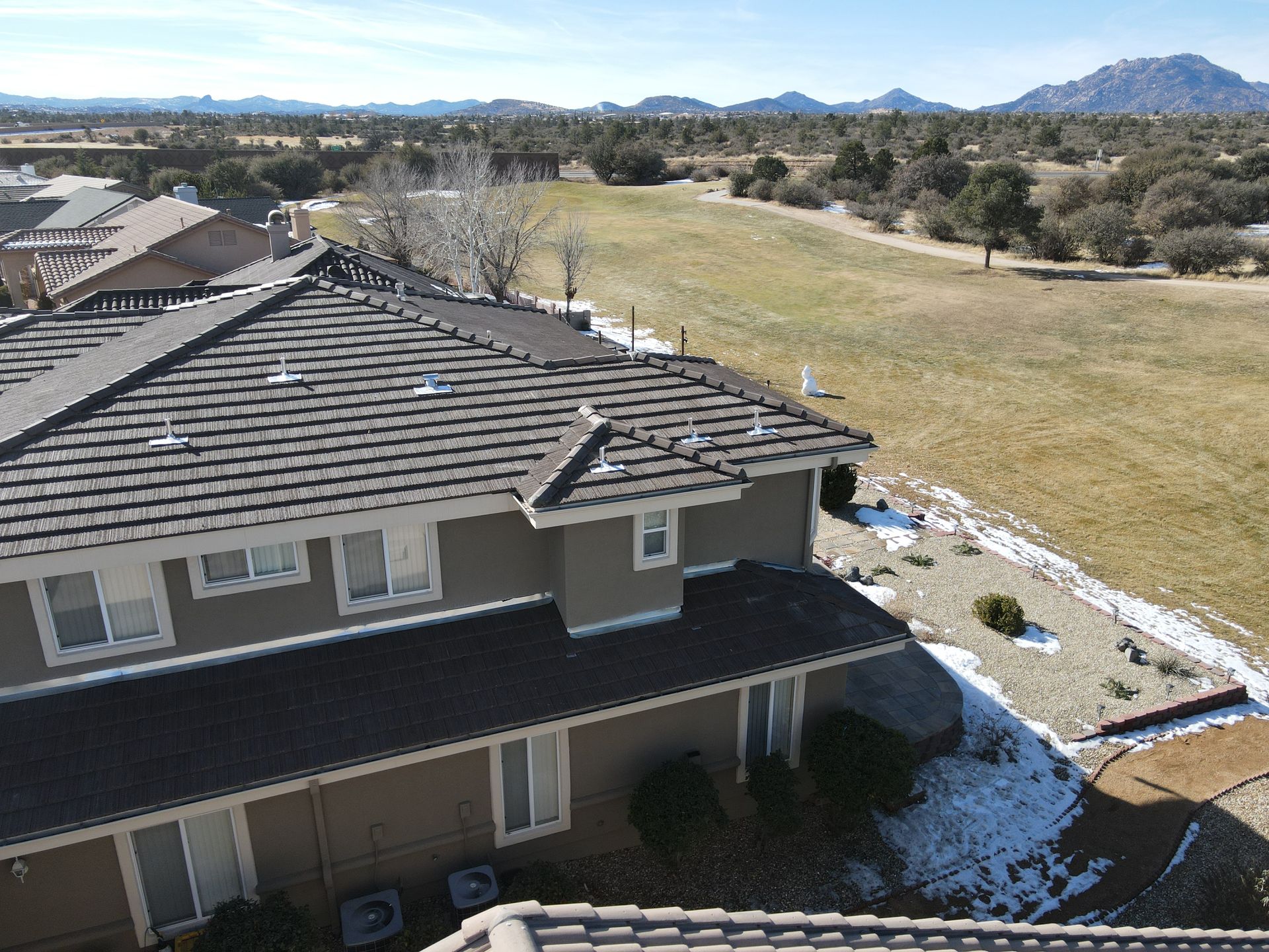An aerial view of a house with a tiled roof and mountains in the background.