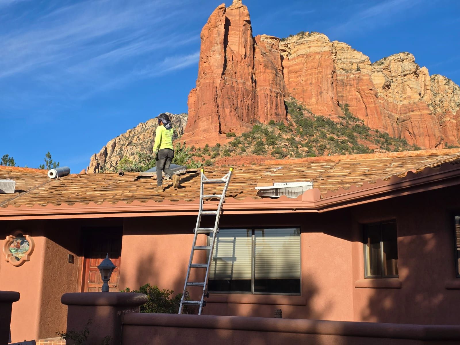 A man is working on the roof of a house with a mountain in the background.