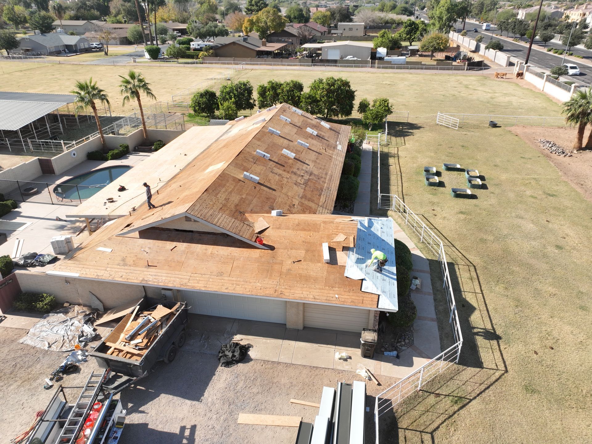 An aerial view of a house under construction with a pool in the background.
