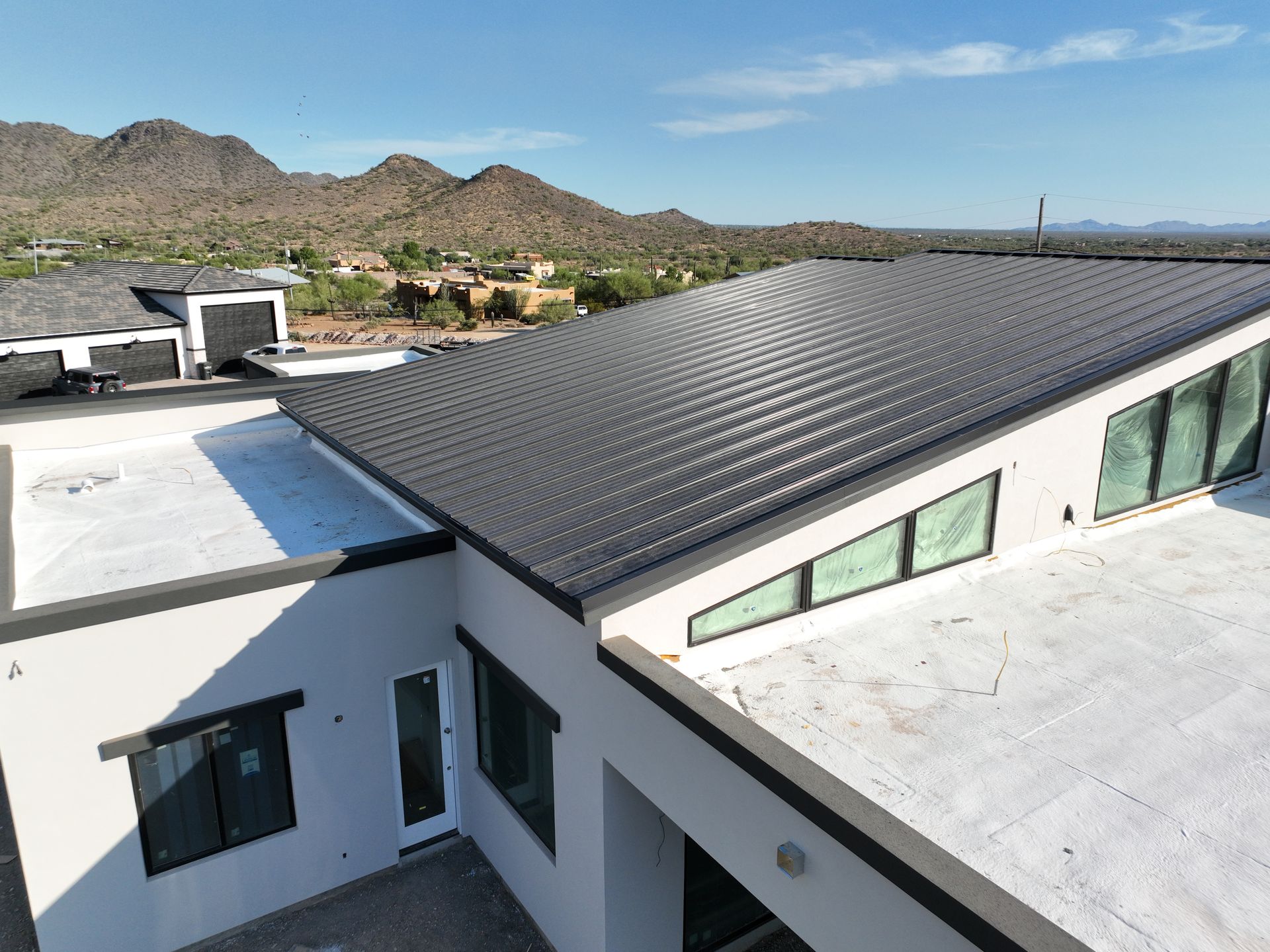A white house with a black roof and mountains in the background.