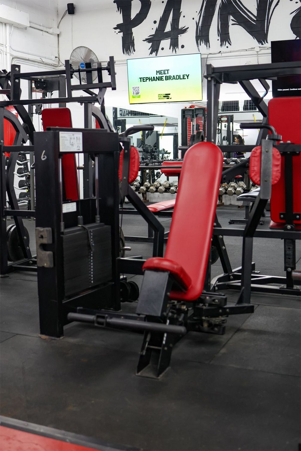 Weight machine with red padding in a gym setting.