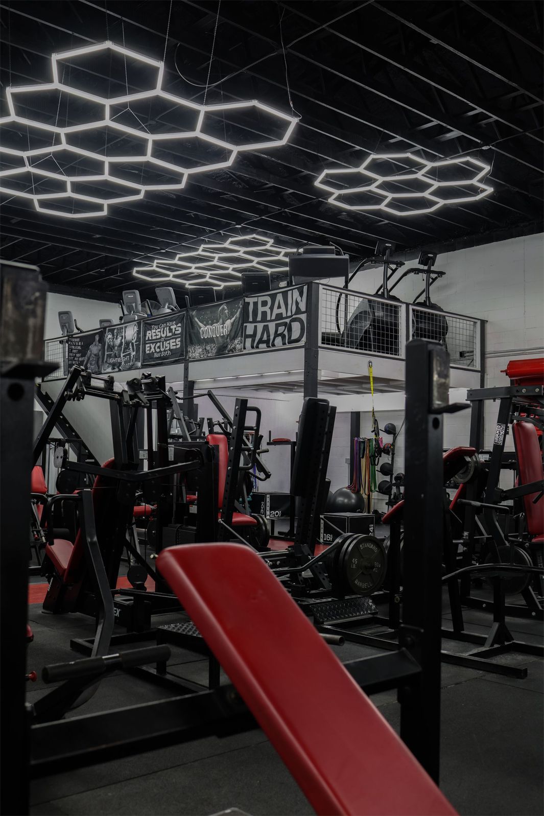 Gym interior with red and black equipment, lit by hexagon-shaped lights.