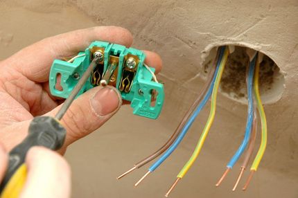 Electrician wiring a green connector to exposed blue and yellow wires in a wall opening