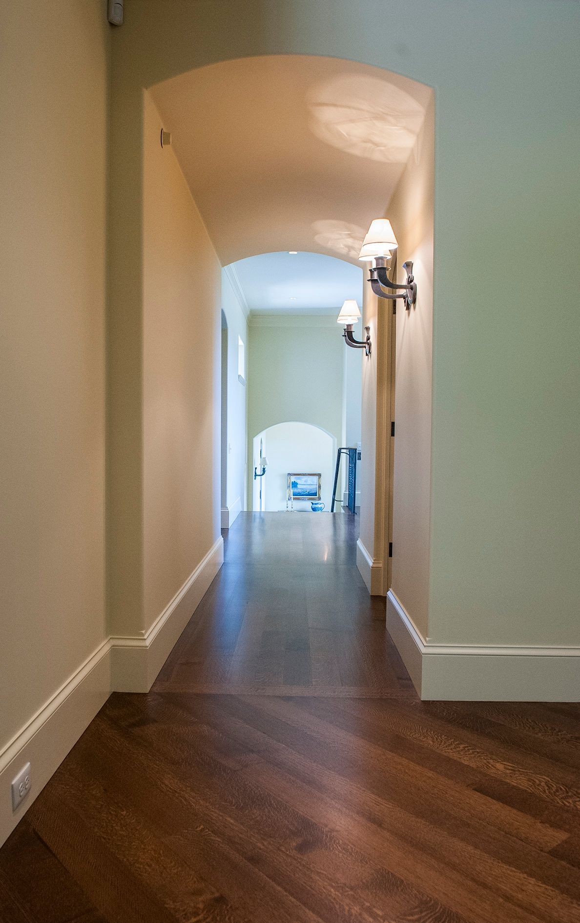 a long hallway with a wooden floor and white trim leading to a living room