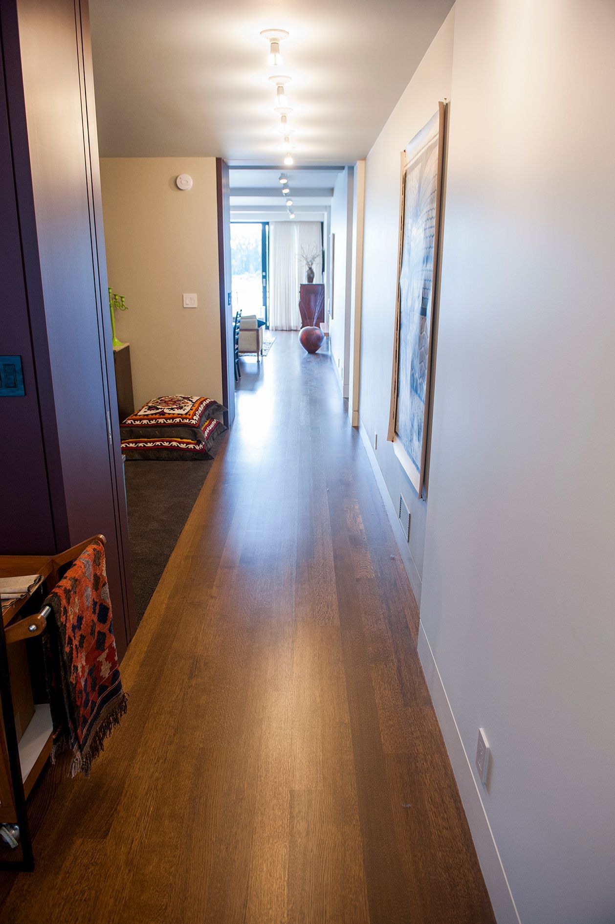 a long hallway with wooden floors and white walls leading to a living room